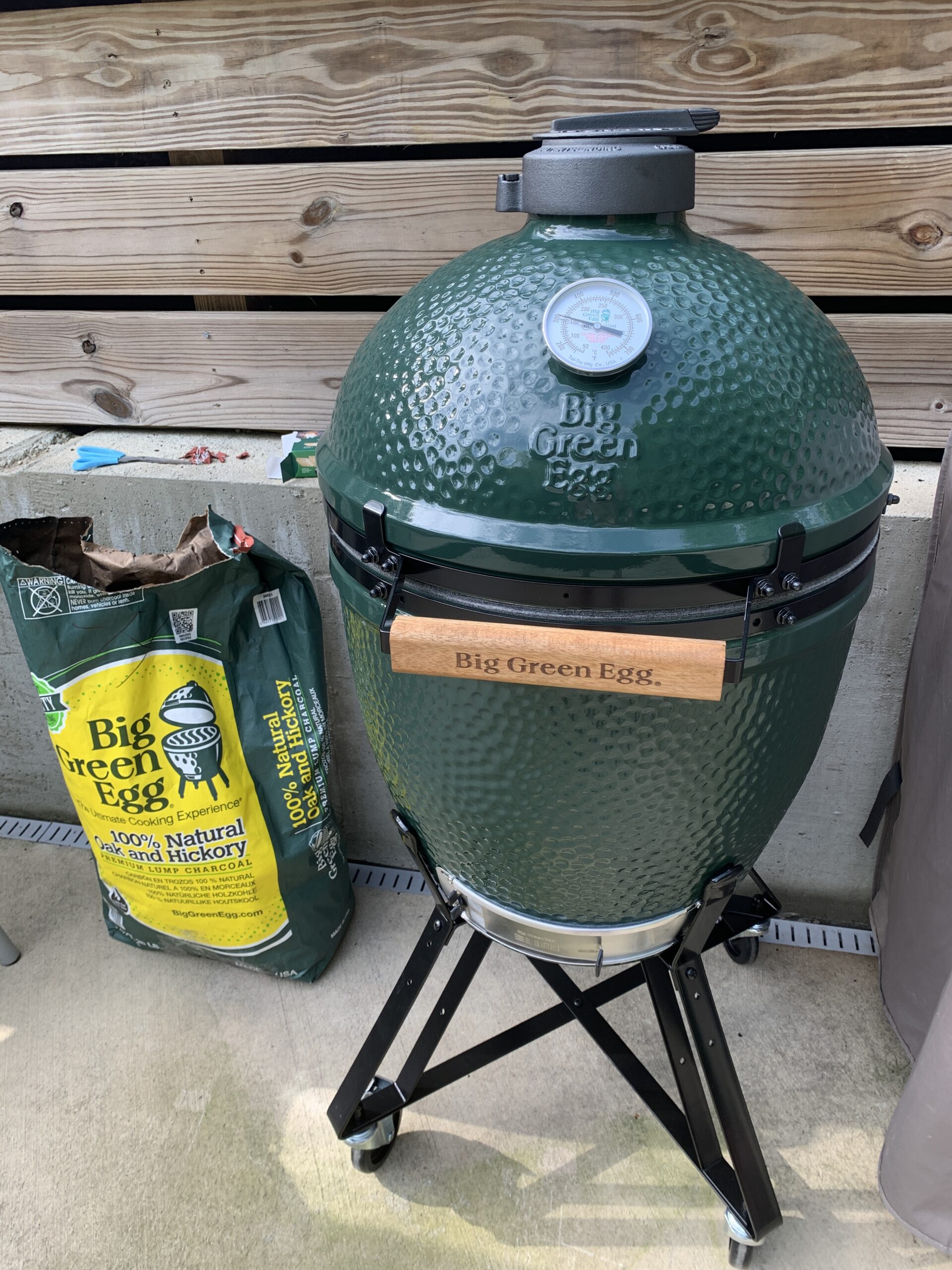 Green smoking grill with a bag of charcoal sitting next to it