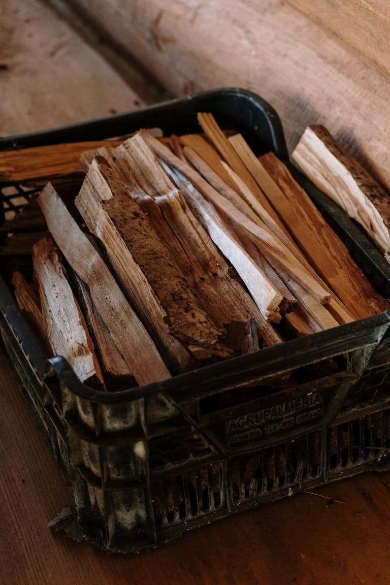 Close-up of rustic wood kindling stored in a black crate indoors, ideal for wood fire use.